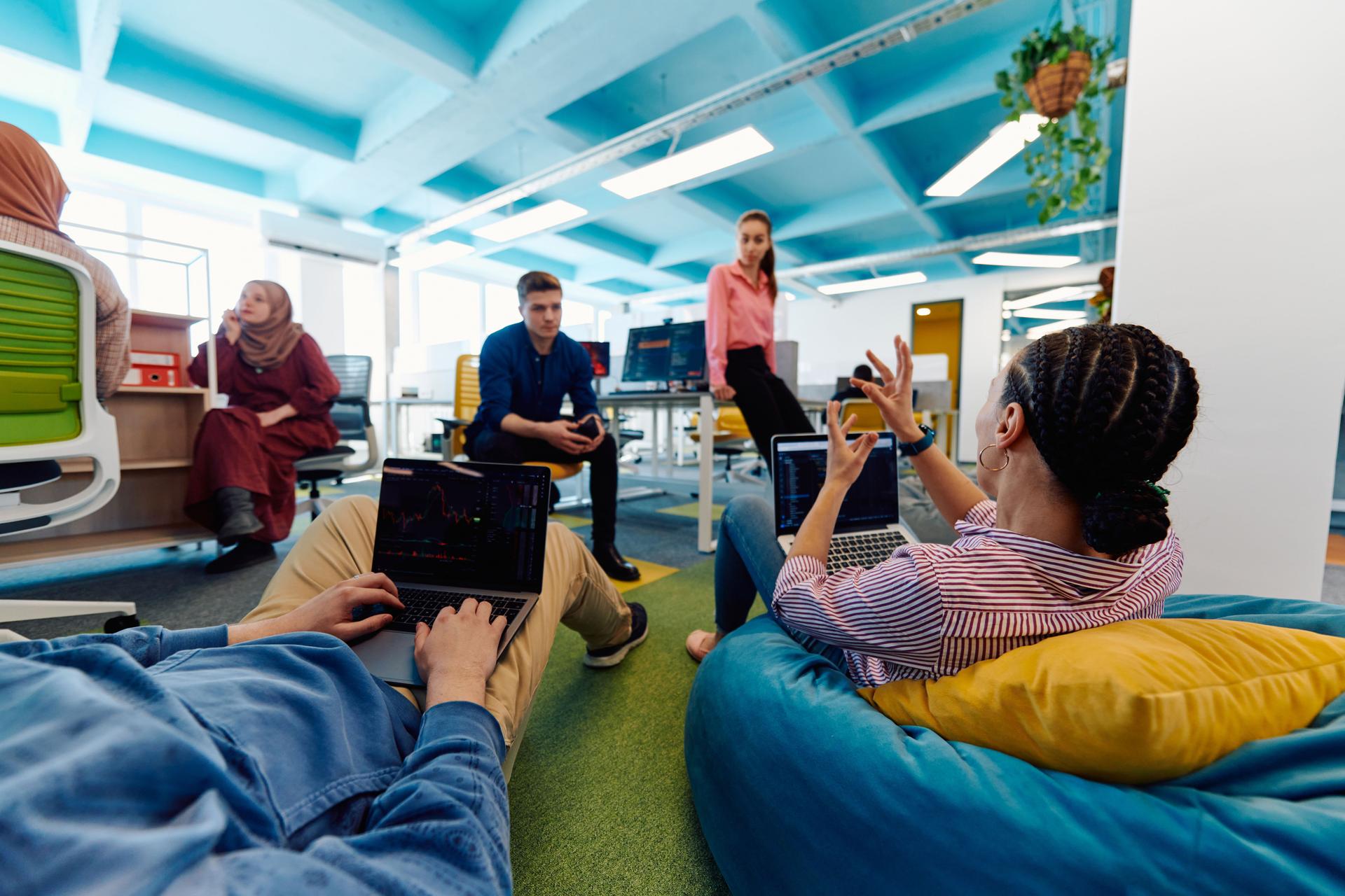 In a modern startup office, a diverse group of young and capable businesspeople engage in lively discussions about various projects, showcasing teamwork, innovation, and entrepreneurial spirit