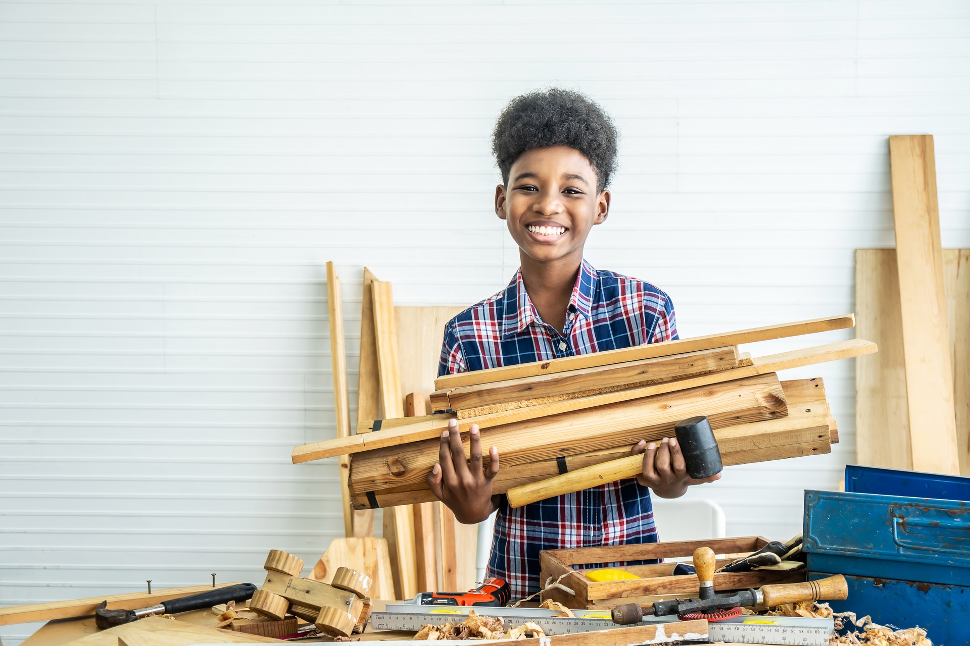 Smiling African-American boy carpenter standing hold several pieces of wood to help father prepare to make woodworking crafts